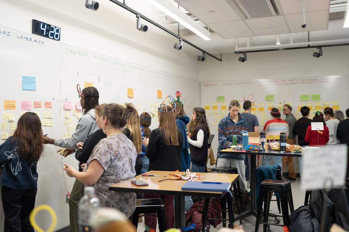 A room of students and Upper Valley educators working at walls of sticky notes