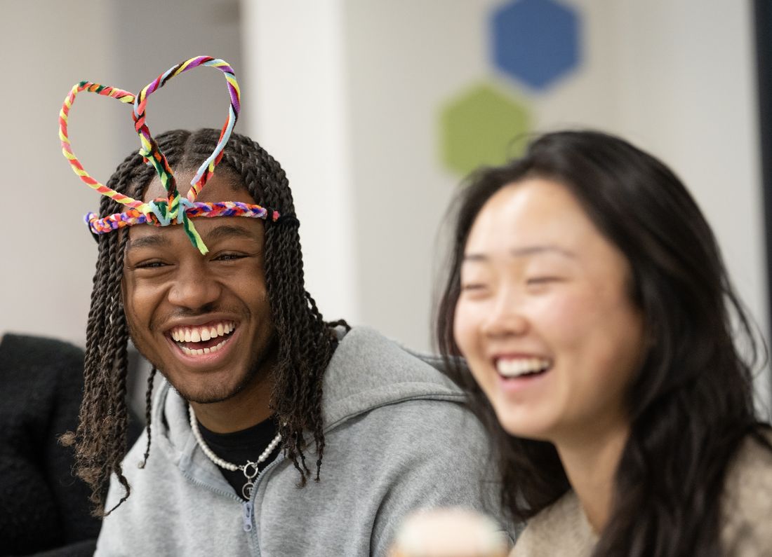 Two students laughing together, one wearing a heart-shaped pipe-cleaner crown