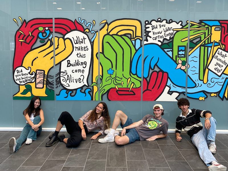 Four students seated in front of the colorful energy-themed mural their Design Corps team created at the Irving Institute